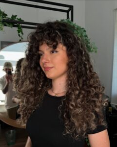 Curly hair, black shirt, indoor setting.