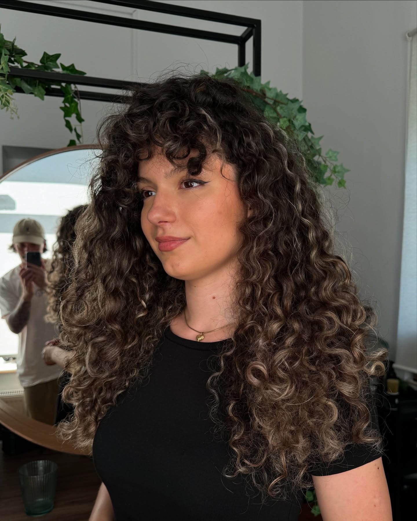 Curly hair, black shirt, indoor setting.